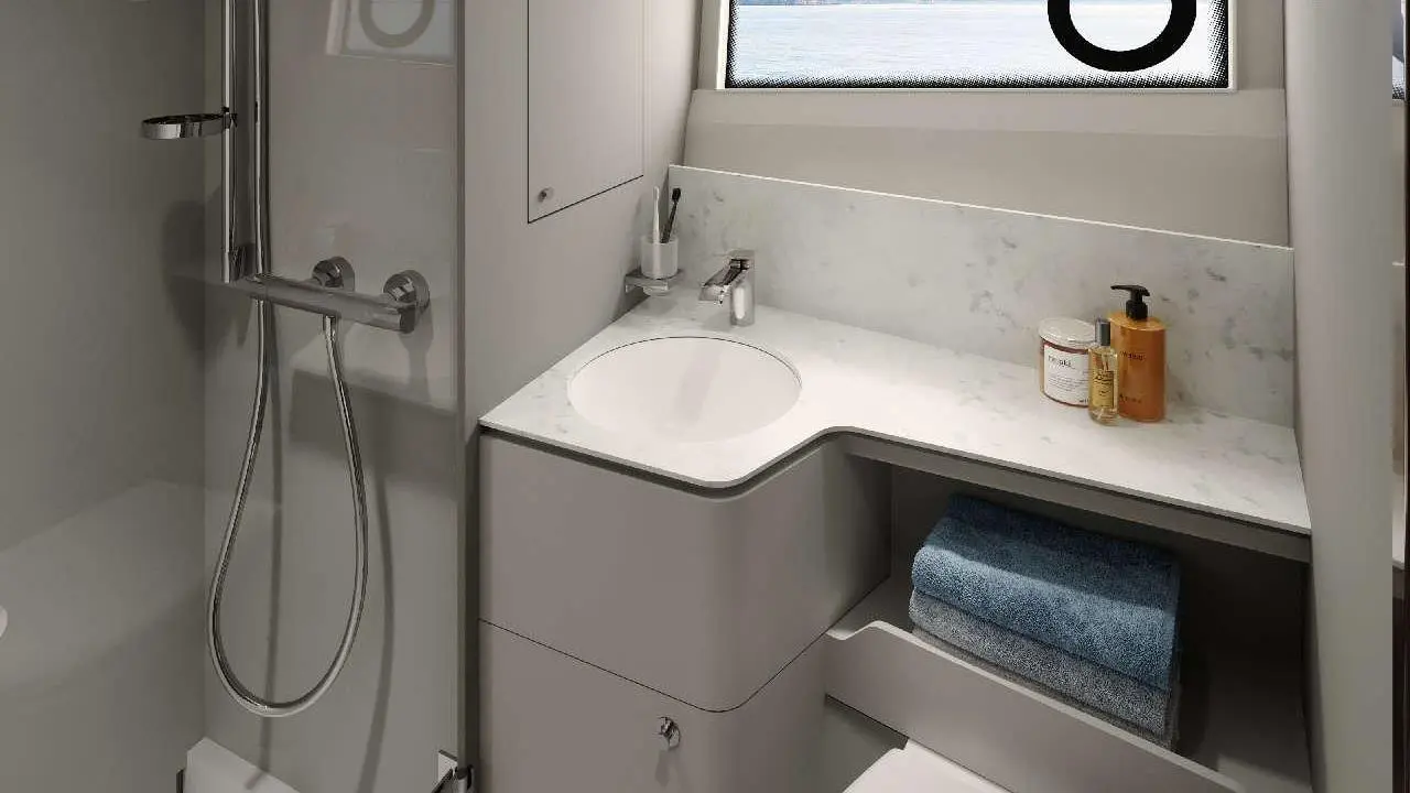 Modern bathroom featuring a shower, circular sink, marble countertop, towel storage, and a scenic ocean view through a circular window.